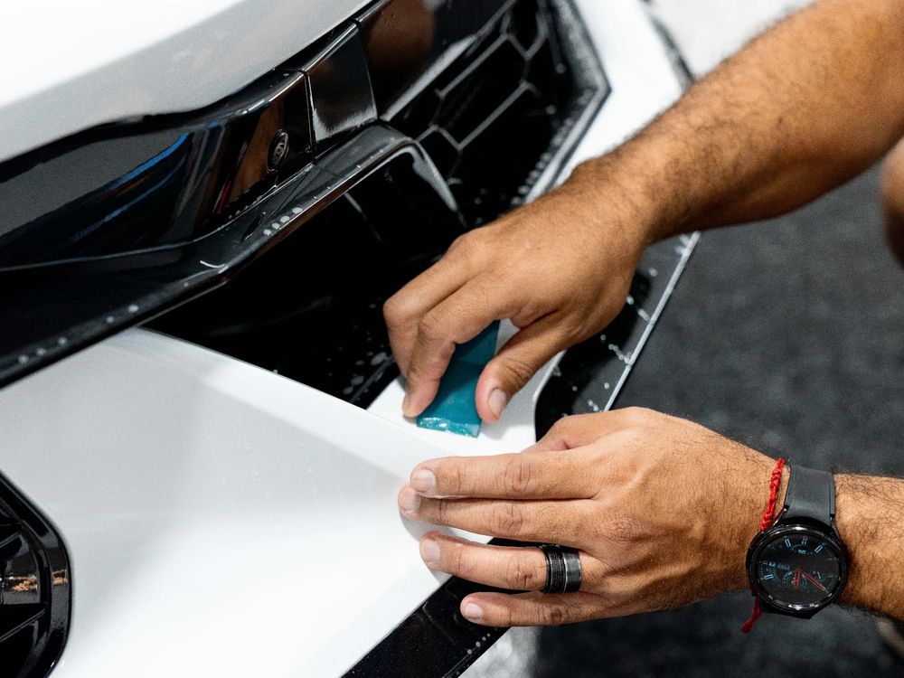XPEL paint protection film being squeegeed onto a white front bumper at Detailers of Ann Arbor
